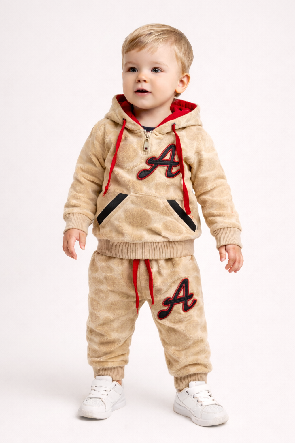 Child wearing a beige hoodie and pants set with red and black accents on a white background